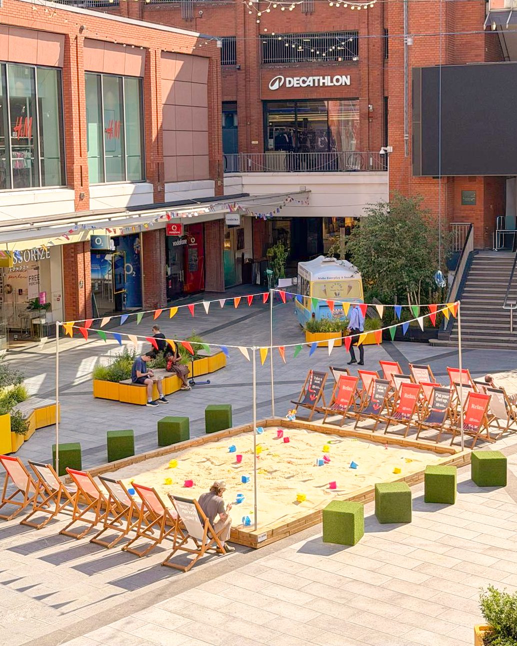 Ealing Broadway town square summer beach installation with sandpit, deckchairs and bunting built by OLLYWOOD