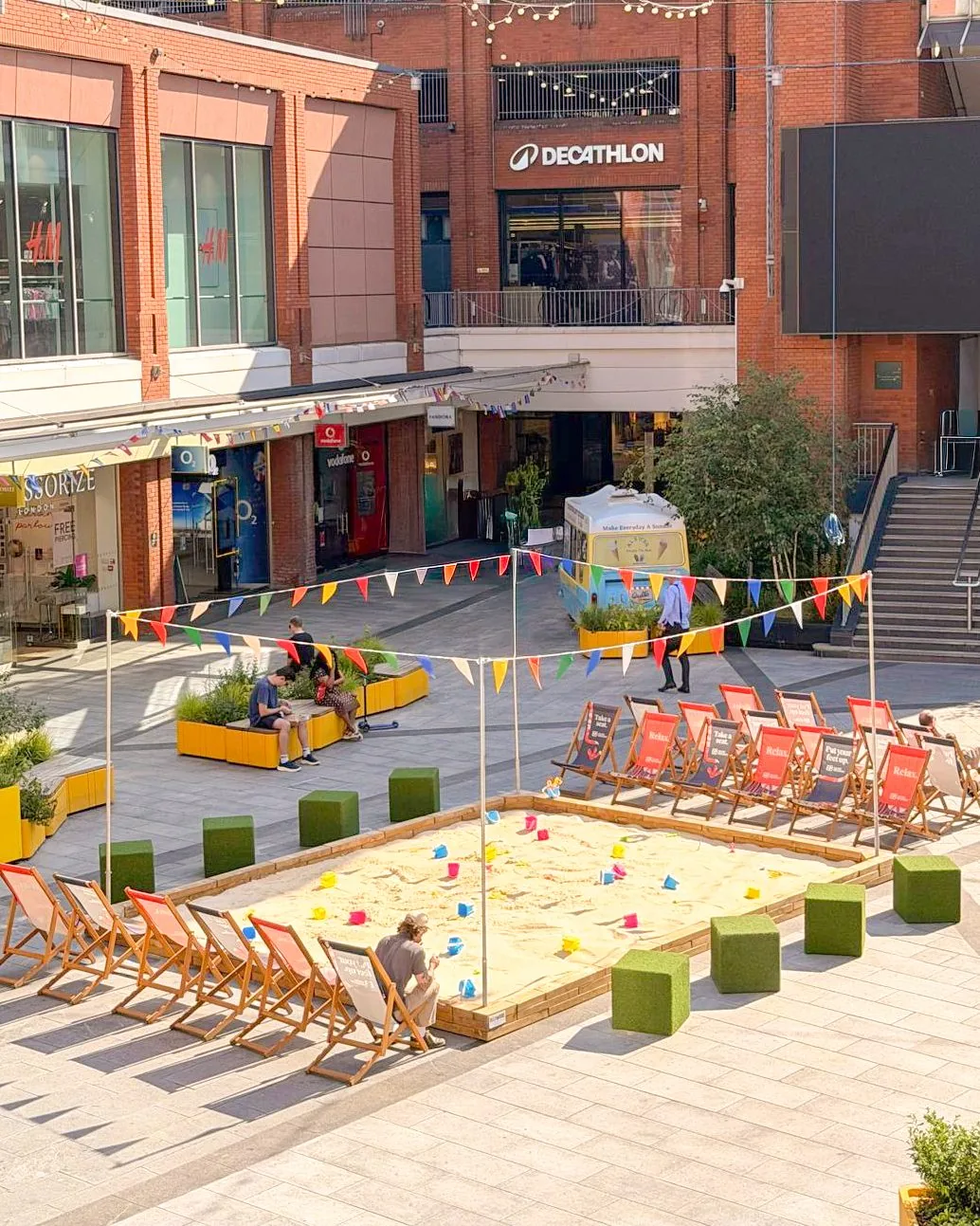 Ealing Broadway town square summer beach installation with sandpit, deckchairs and bunting built by OLLYWOOD